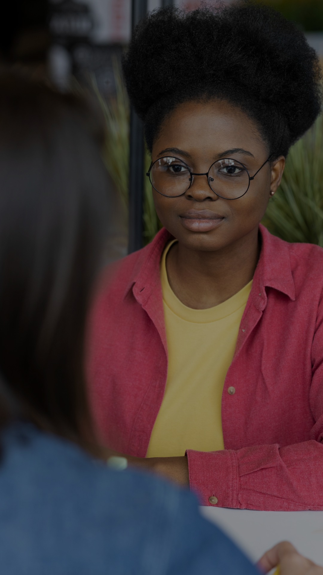 A young woman of color sits with another student at a table.