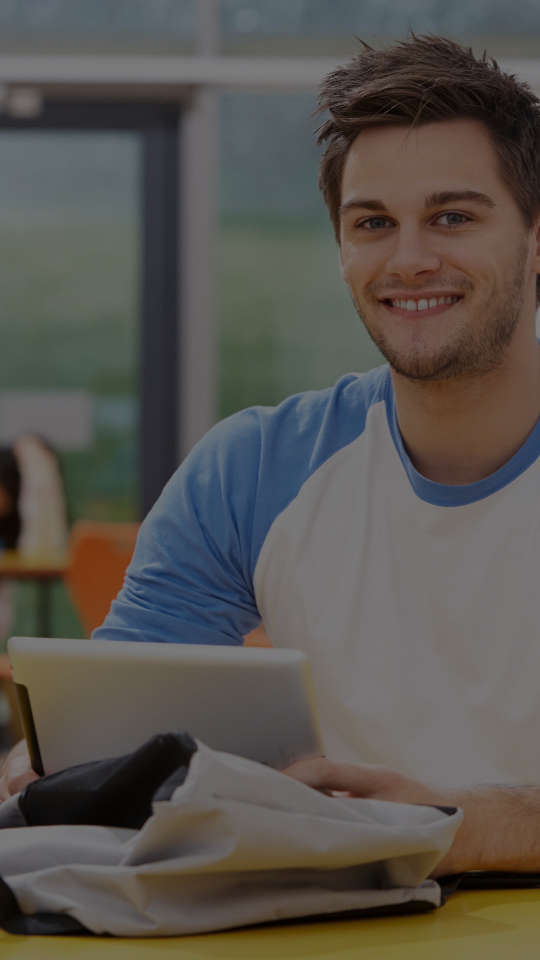 A young man wearing a baseball tee sits with his laptop open.