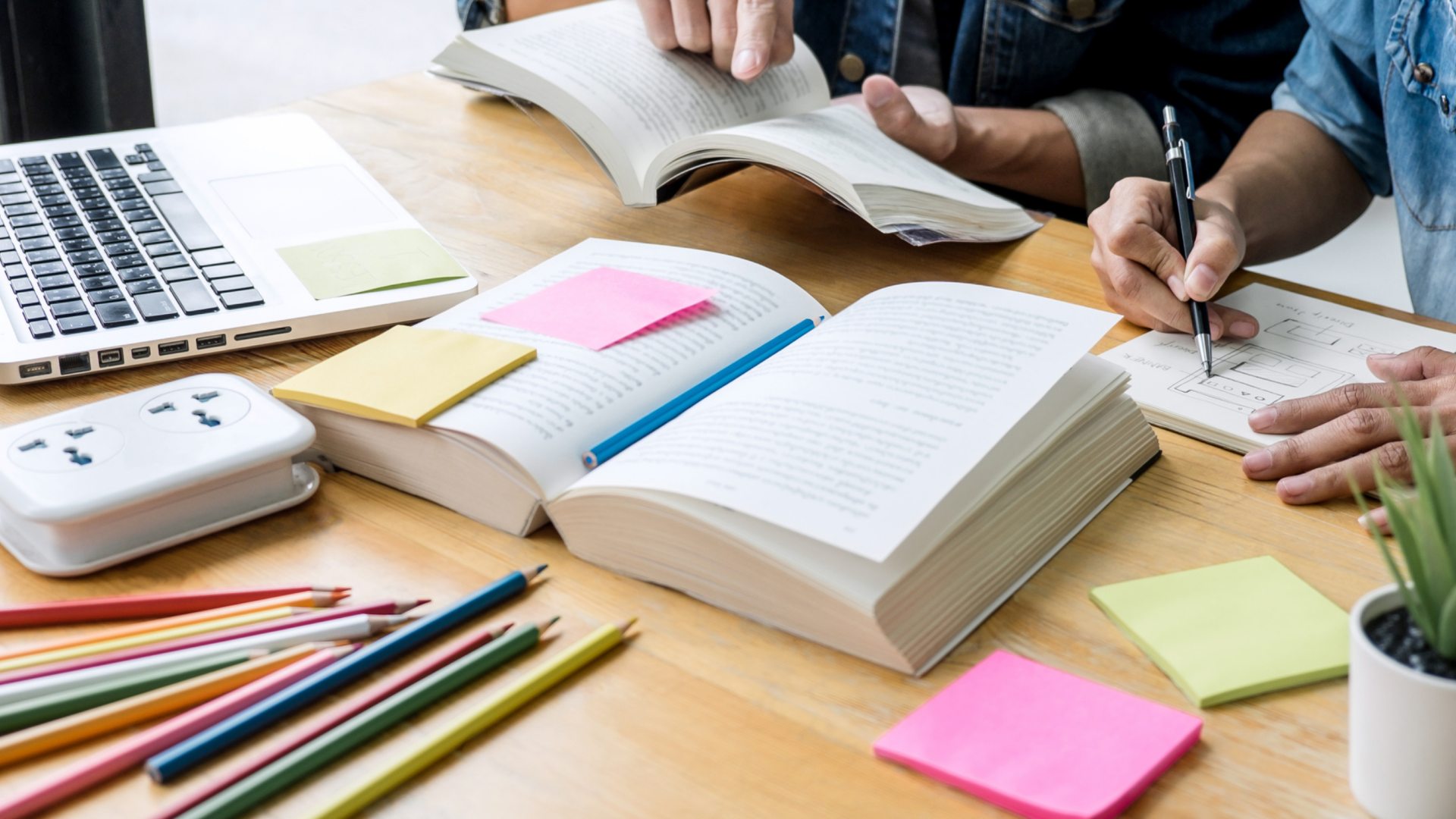 Open laptop and textbook surrounded by notes and colored pencils.