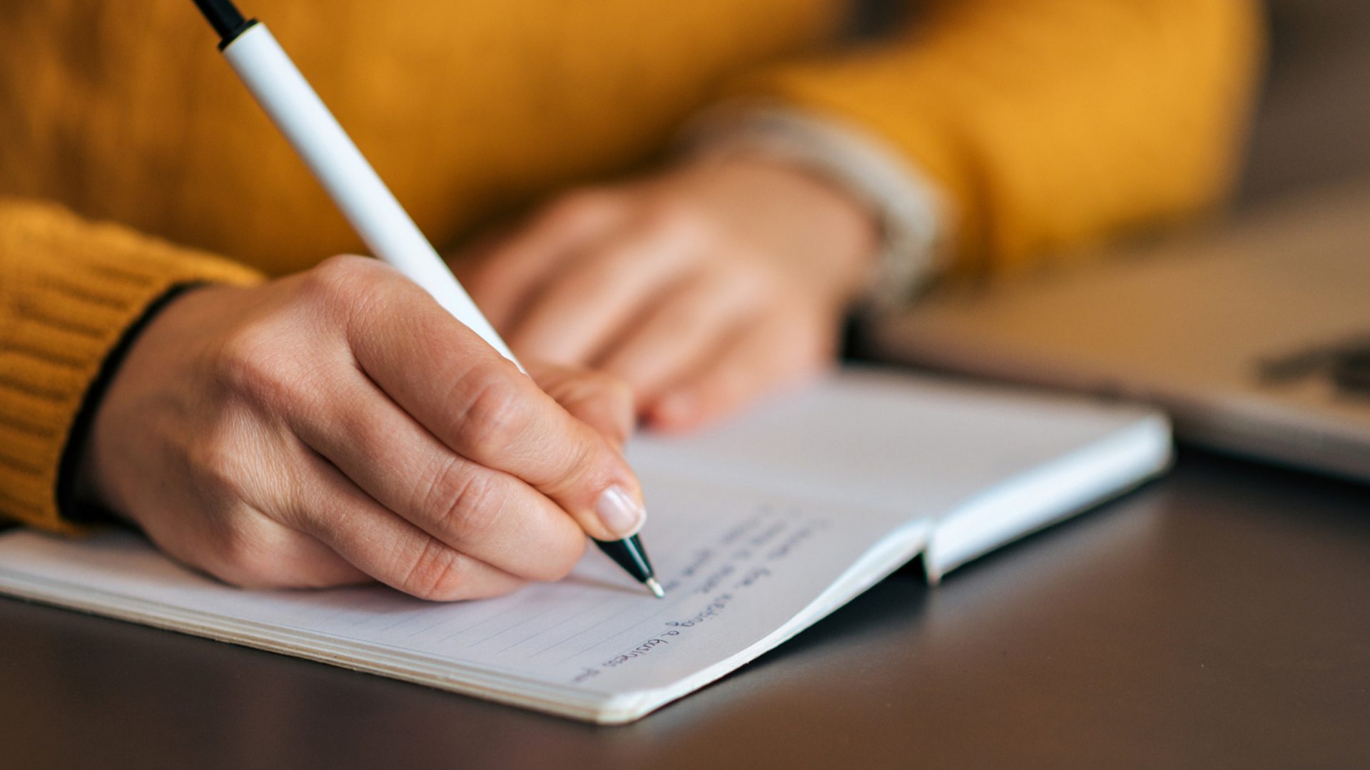 Woman in yellow sweater writing in a journal.