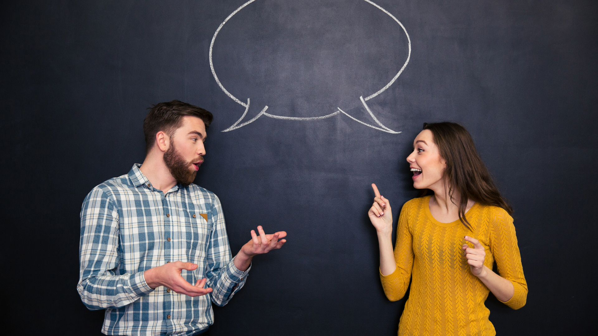 A man and woman talk in front of a blackboard.