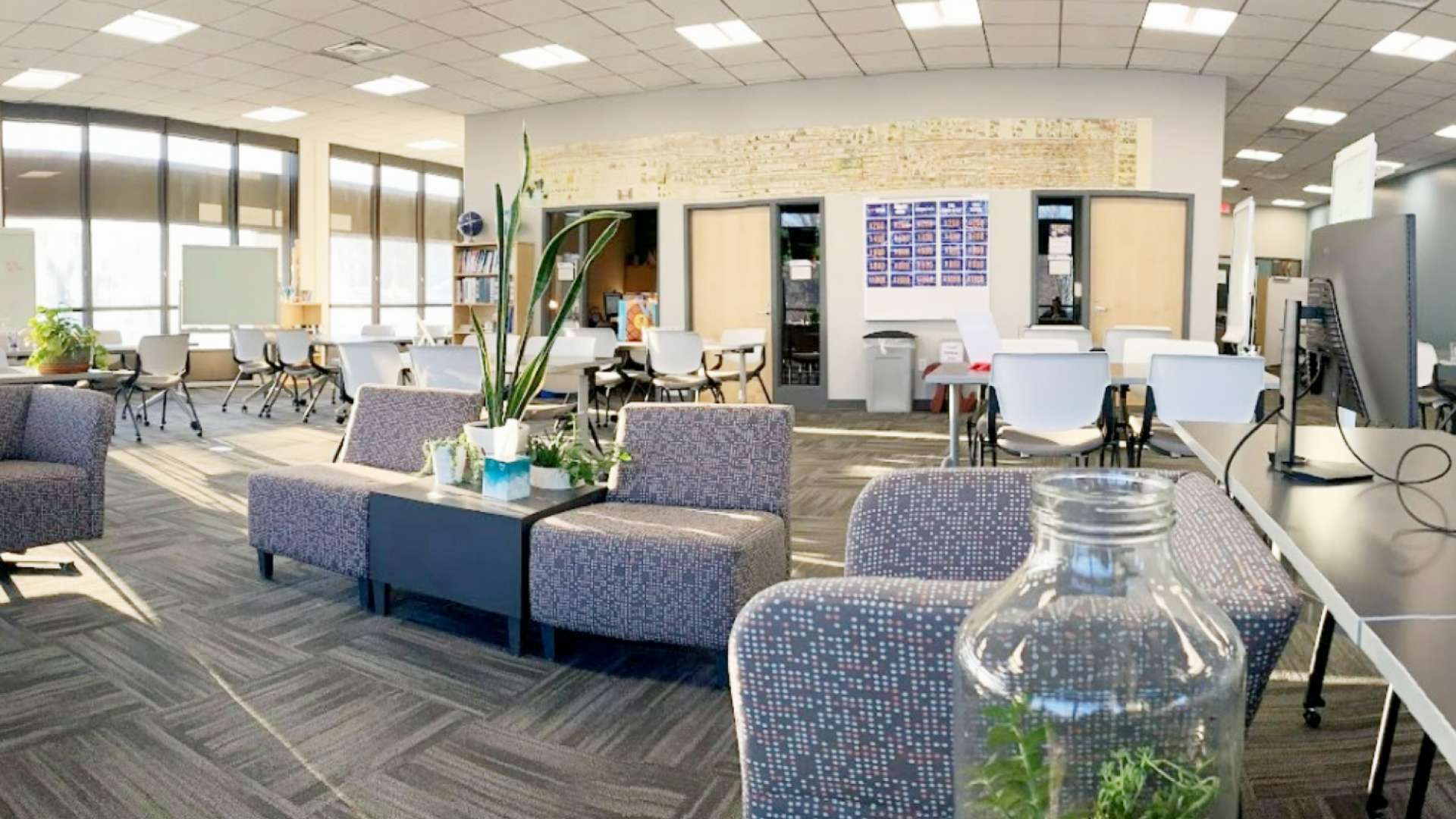 Sunshine filled learning space with soft furniture, green plants, tables and chairs.