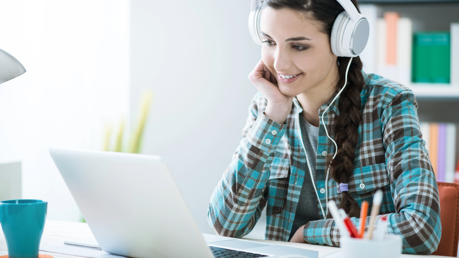 A young woman wearing headphones smiles and watches a class on her laptop. 