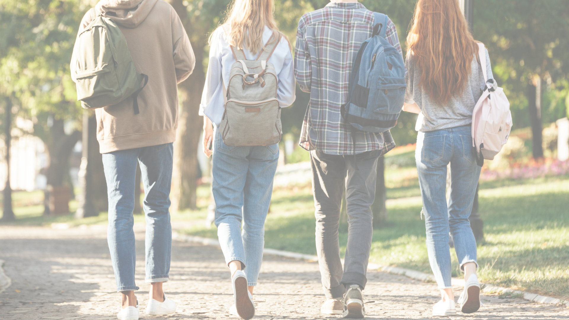 Four college students walk on a brick path on a sunny, summer day. They are carrying backpacks and headed toward a building. 