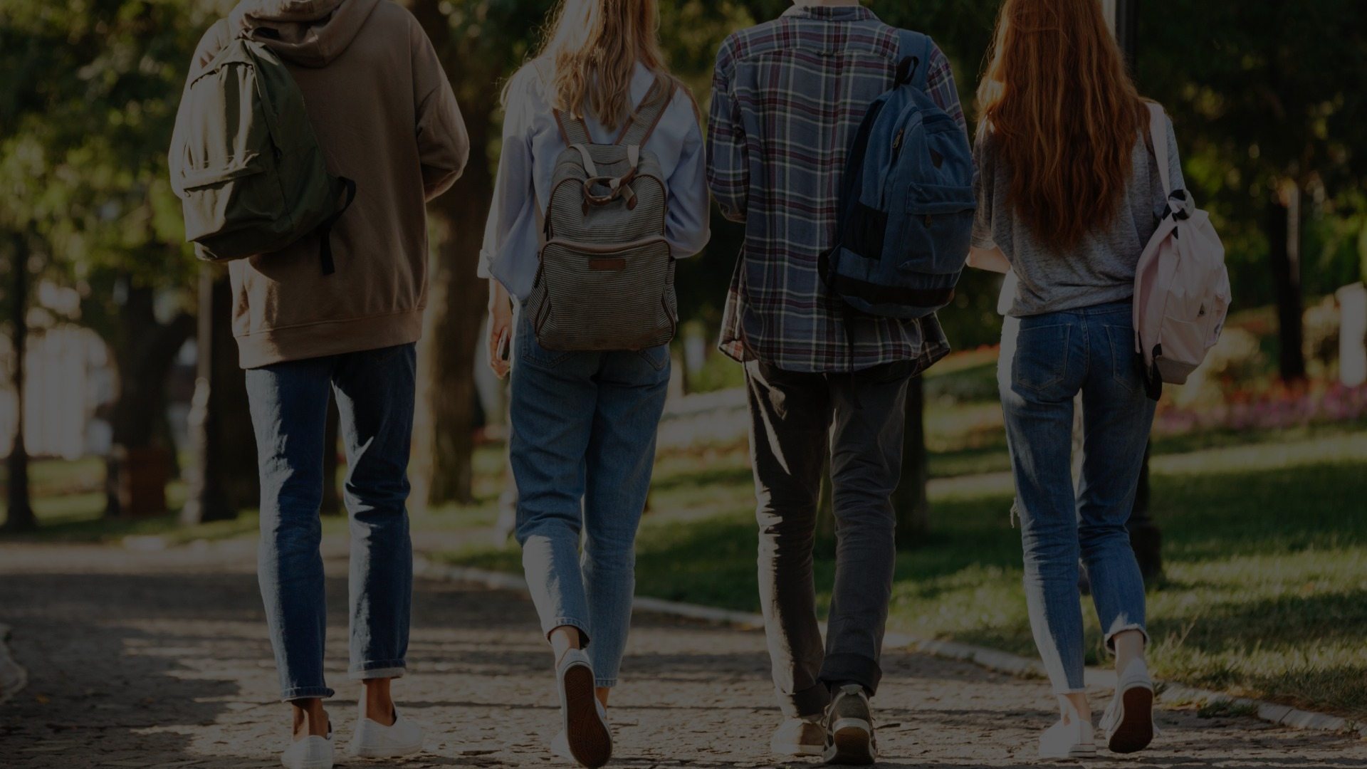 Group of four young adults walking together in the sunshine wearing backpacks.
