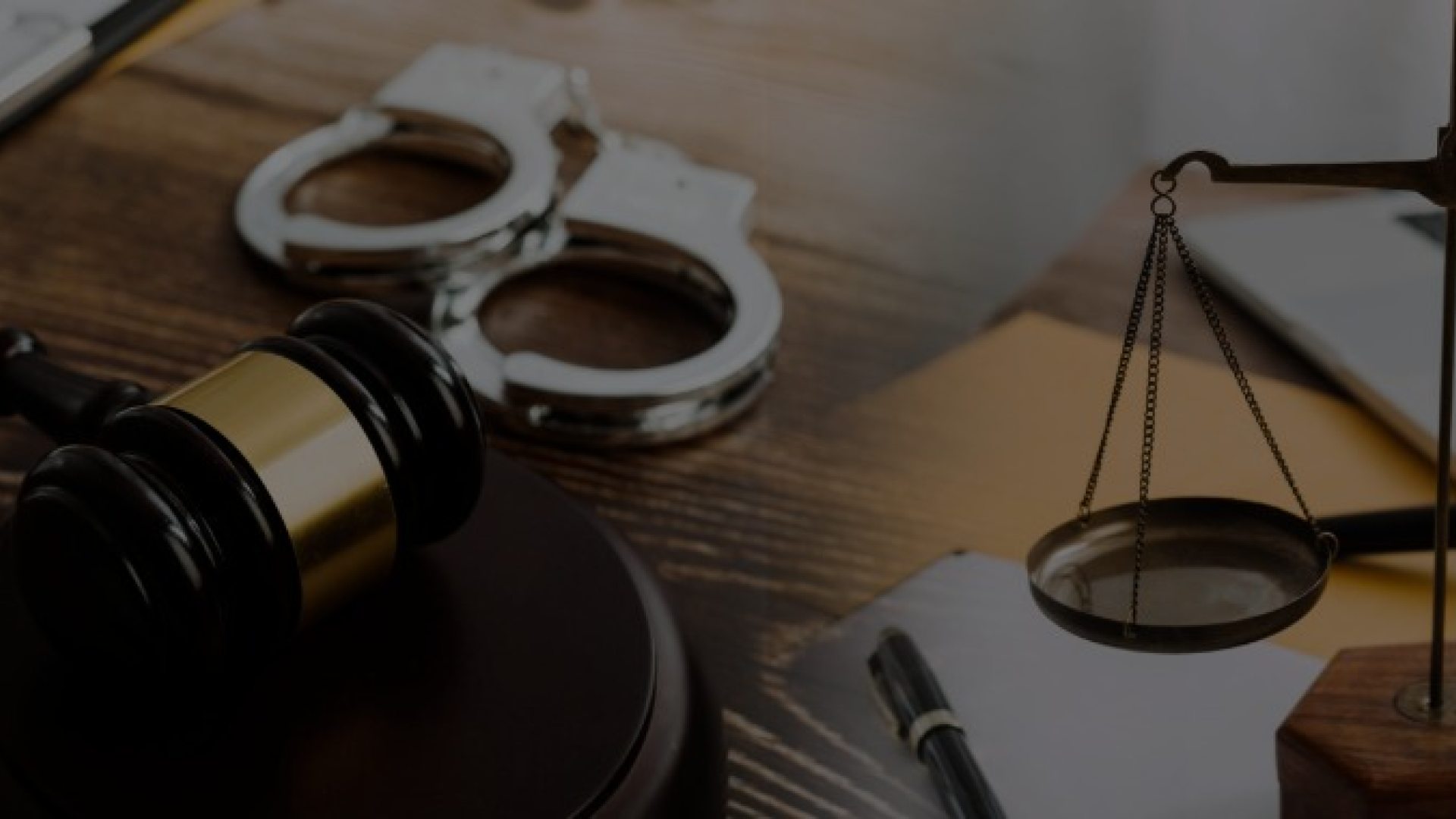 Handcuffs, a gavel and scale of justice are displayed on a wooden desk.