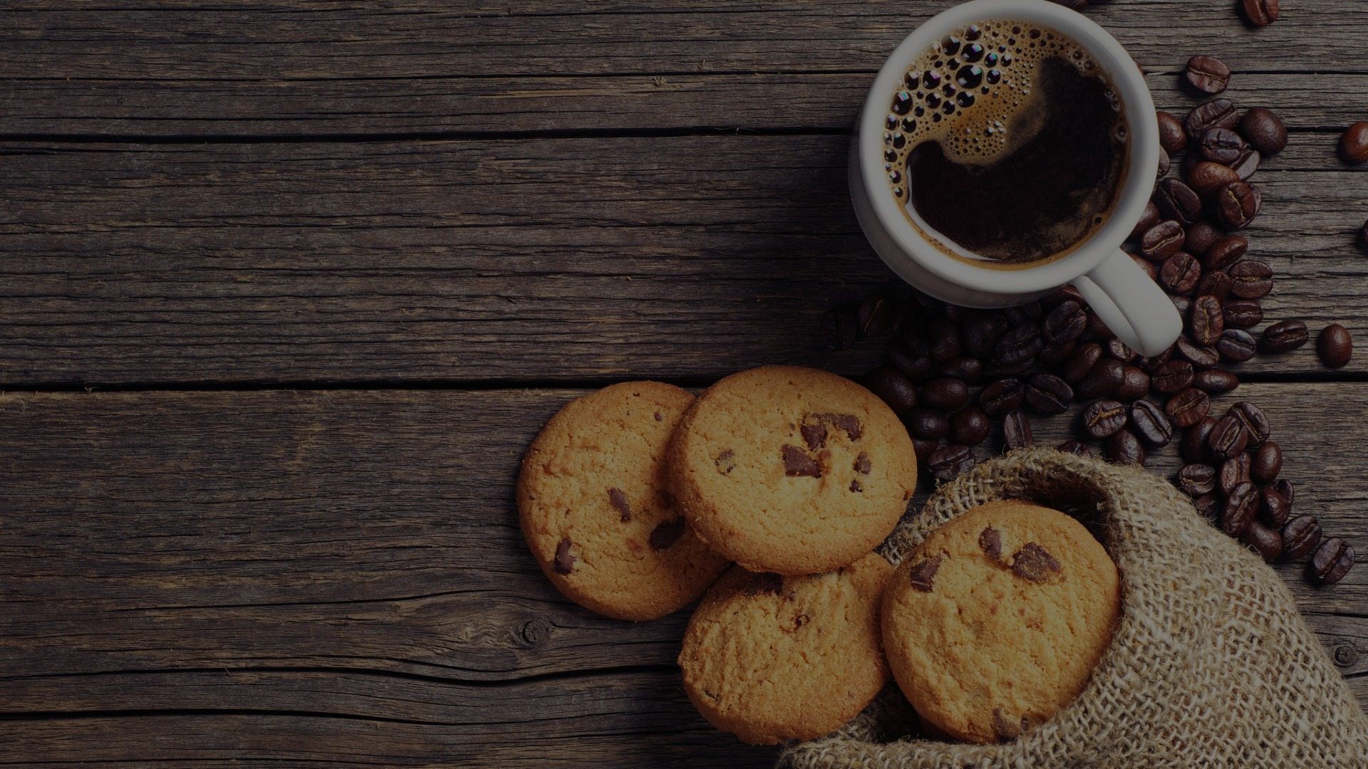 A cup of coffee and pile of chocolate chip cookies is laid on a table.