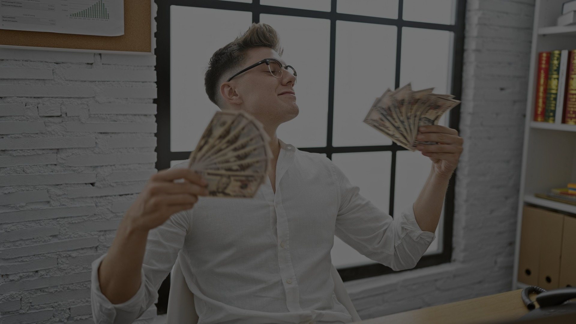 A man fans himself with two piles of cash.