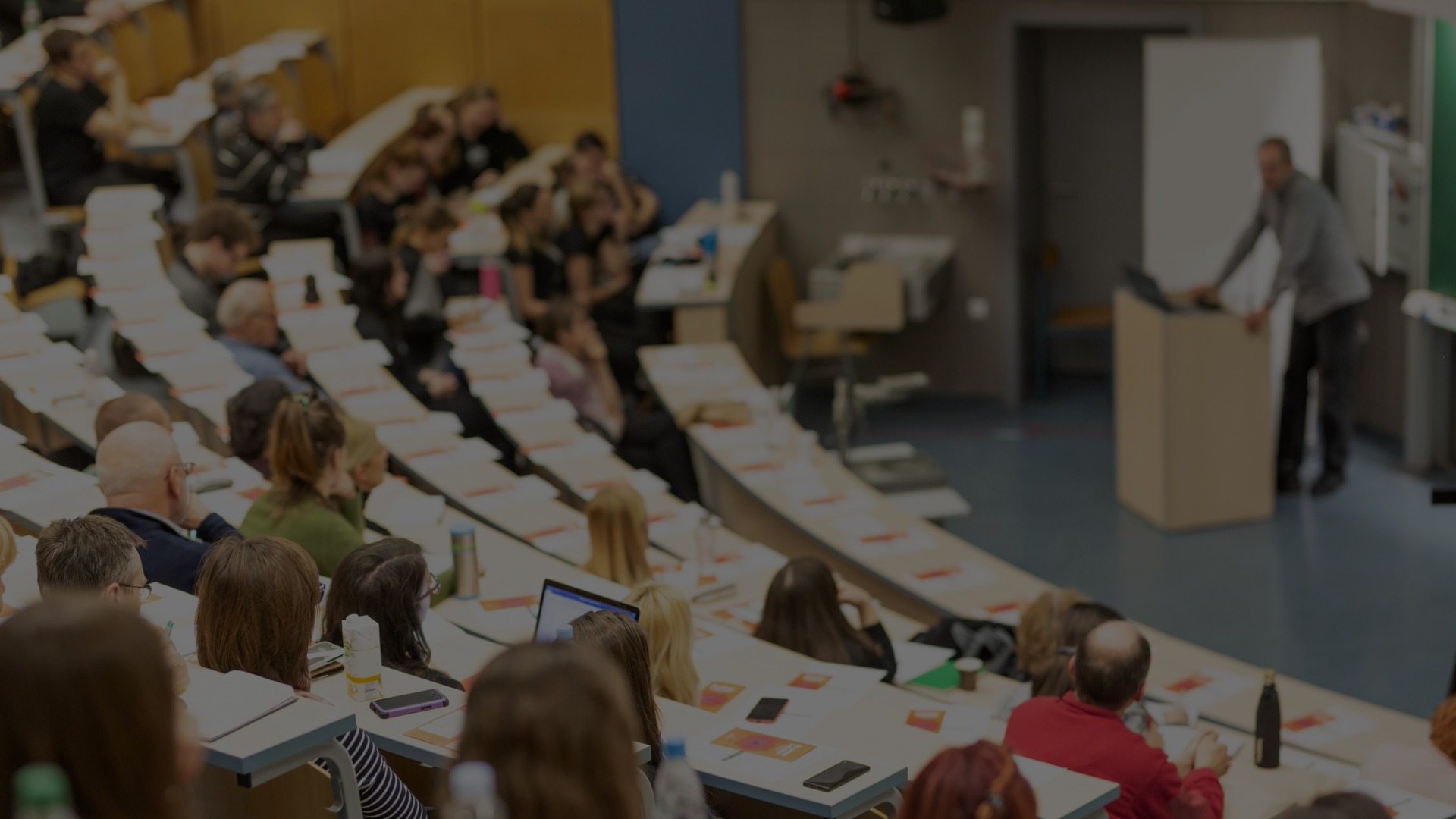 A tiered lecture hall full of students listens to a professor.