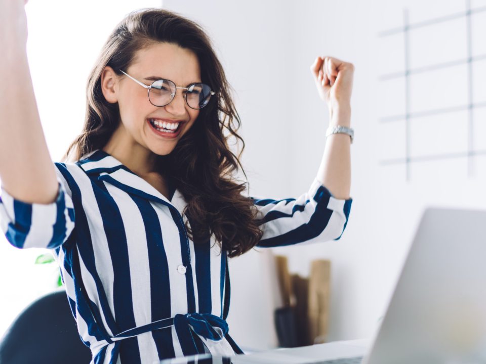Young woman cheering about happy results on laptop.