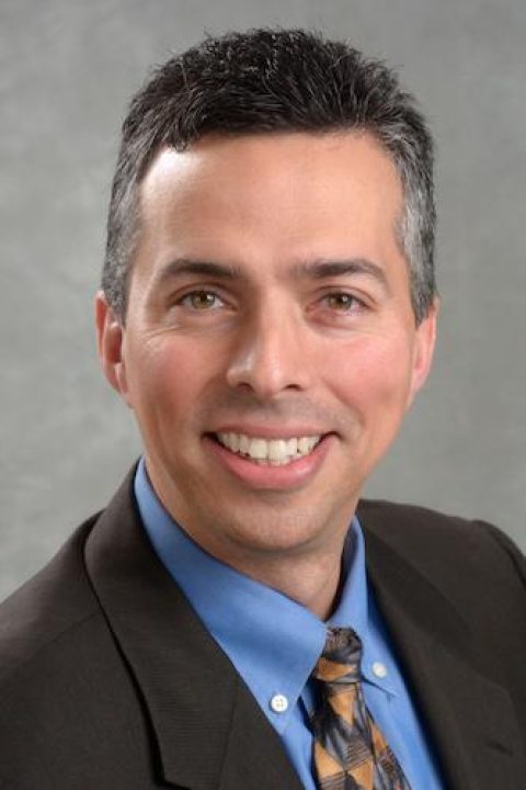 Portrait of William Bowers, a man with short dark hair, wearing a blue shirt and patterned tie, smiling at the camera.