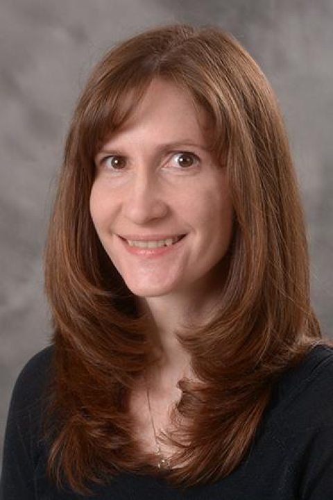 Portrait of Julie Marte, a woman with long straight brown hair, wearing a dark top, smiling at the camera.