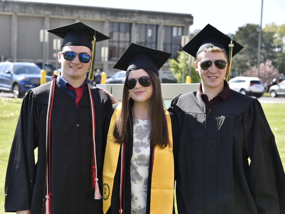 Three students wearing sunglasses and commencement regalia