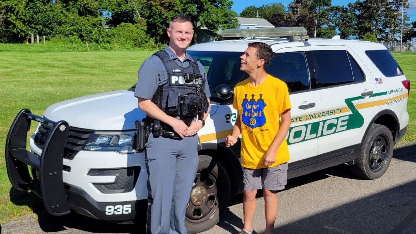 A student standing with a University Police office in front of a police car
