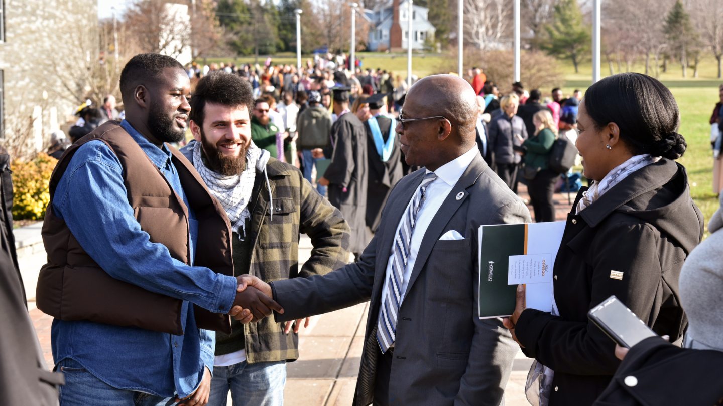 President Nwosu shakes hands with 2022 graduate Yahya Ndiaye while people congregate outside the Marano Center after the December commencement ceremony