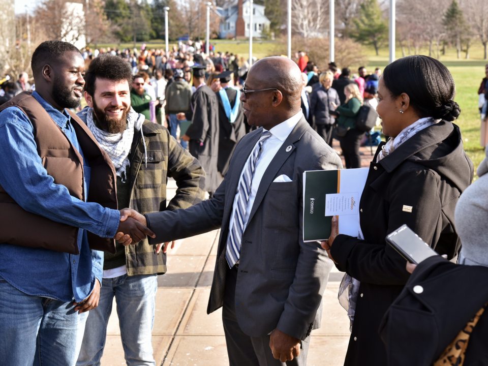 President Nwosu shakes hands with 2022 graduate Yahya Ndiaye while people congregate outside the Marano Center after the December commencement ceremony