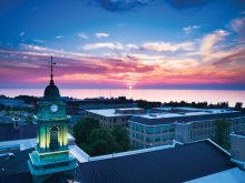 An aerial view of a sunset over the Oswego campus and the Sheldon Hall cupola with Lake Ontario in the background.