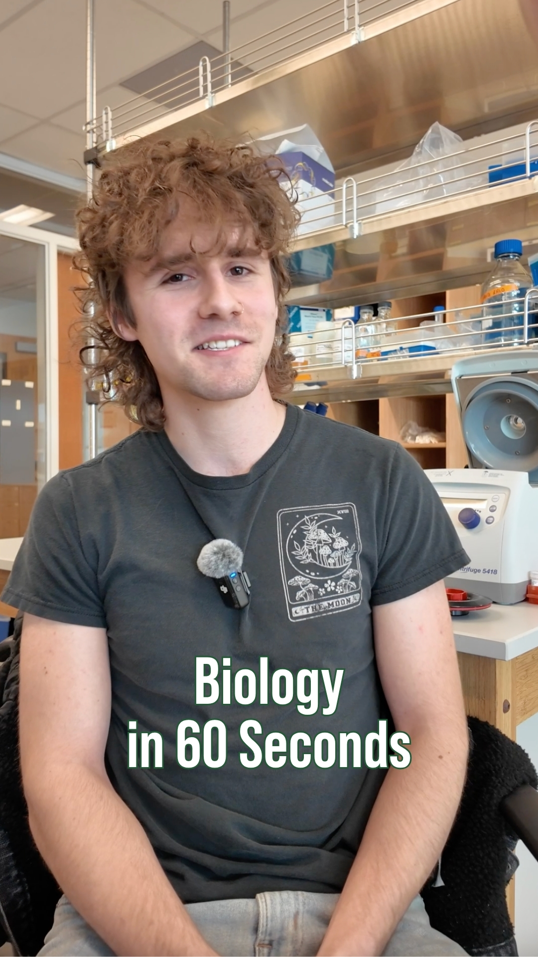 A student wearing a microphone sits in a biology lab with scientific equipment in the background, with on-screen text reading “Biology in 60 Seconds.”