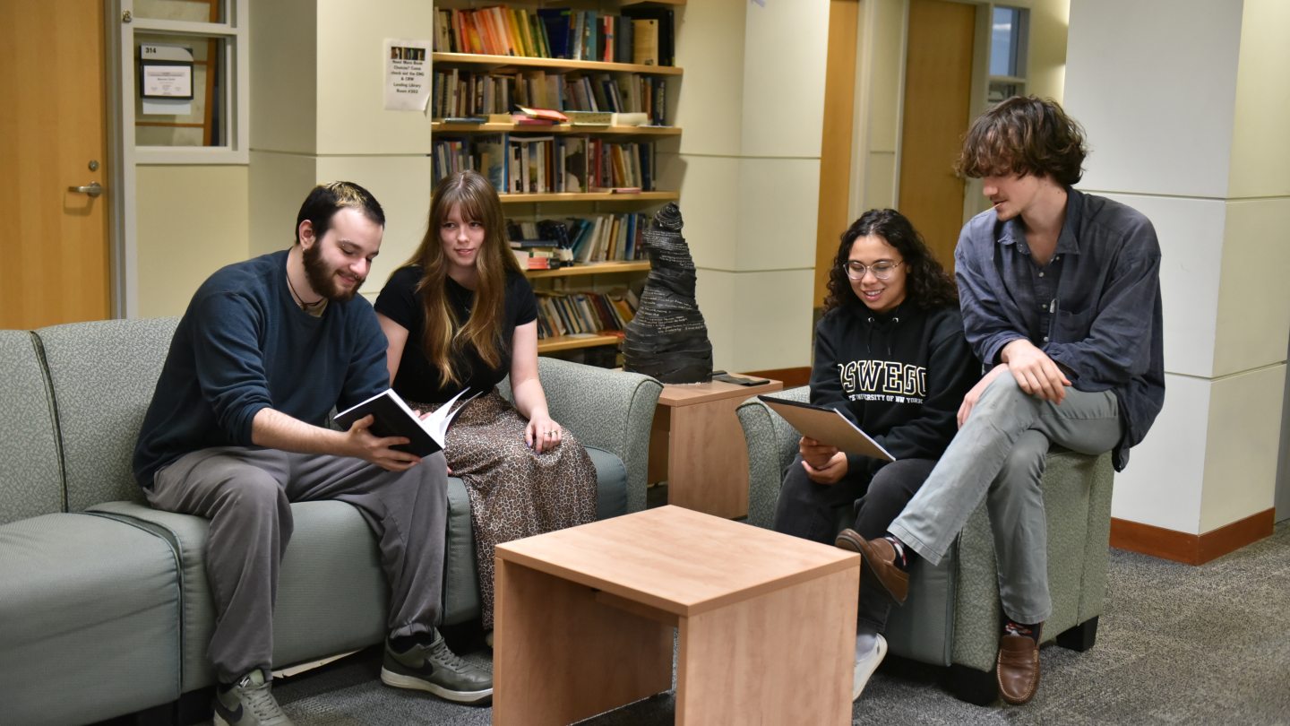 Four students sitting on couches in a lounge, with bookshelves behind them