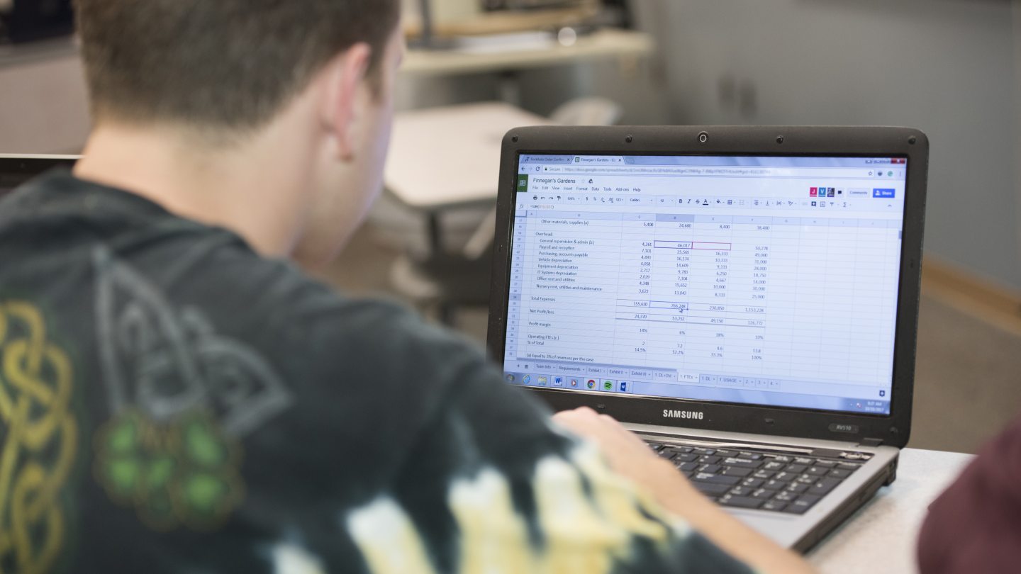 male student typing on a laptop with an excel file open