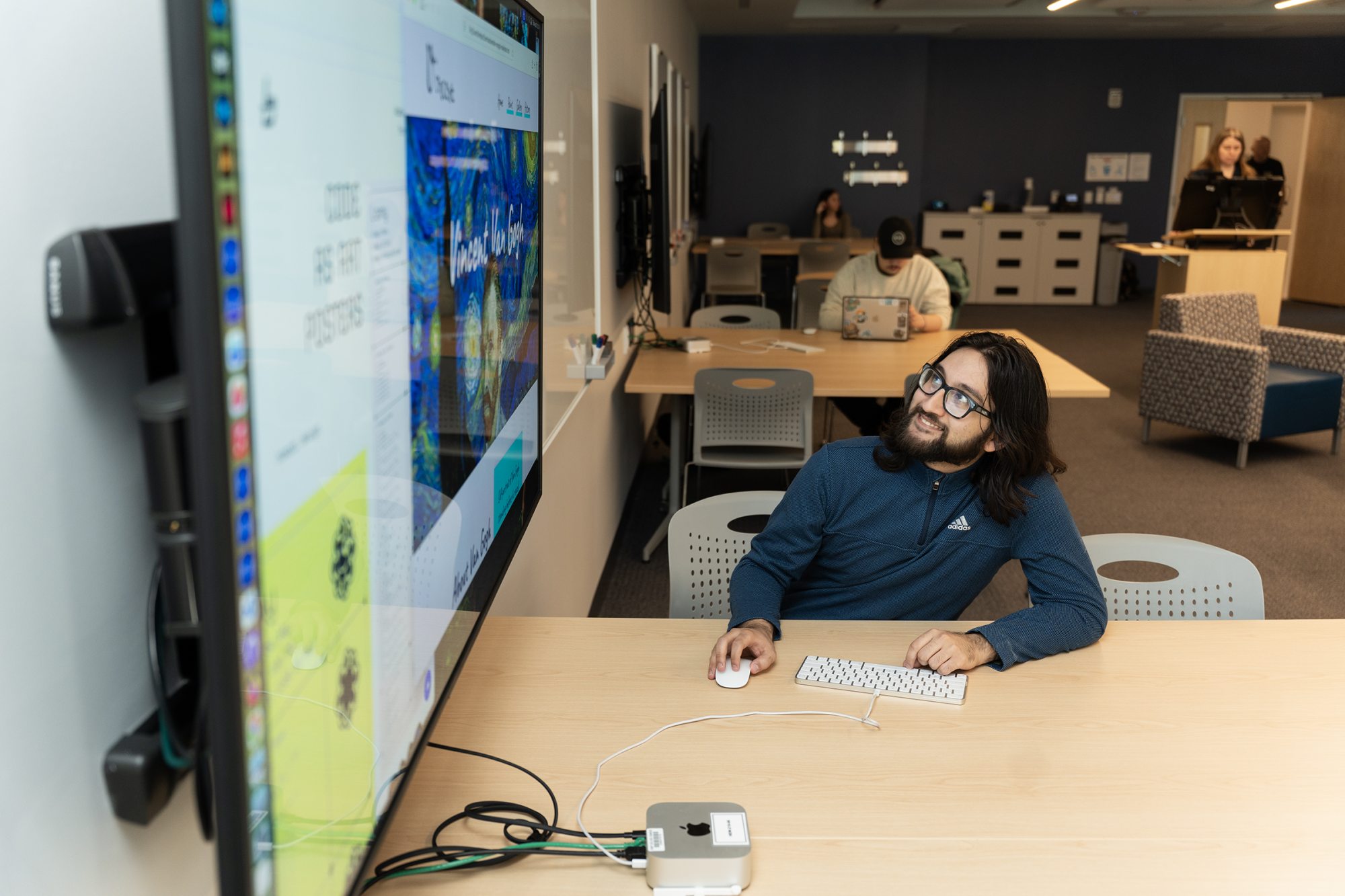 A graphic design student uses digital design tools and a large display to develop creative projects in a studio learning environment.