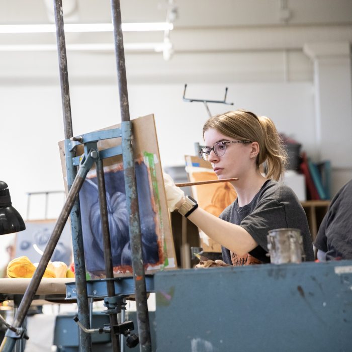 An art student paints at an easel during a studio art class.