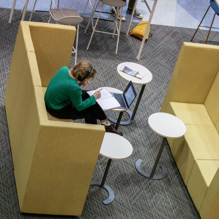 A student writes in a notebook with an open laptop nearby.