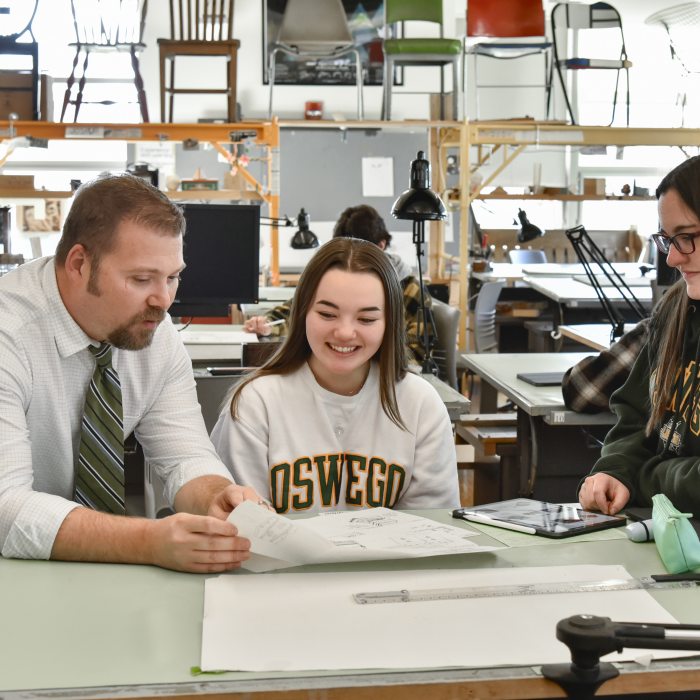 Professor and two students looking at blueprints at a drafting table.