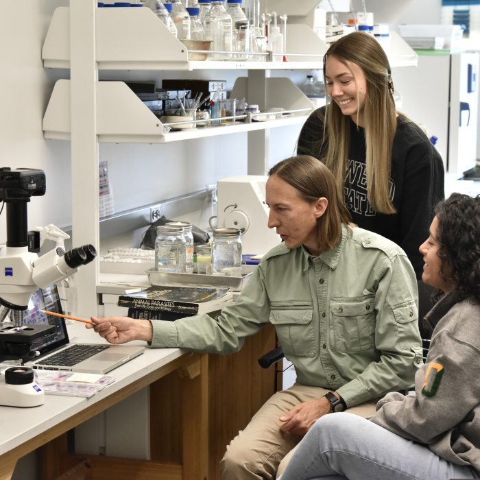 Faculty member working with two SUNY Oswego students as they examine specimens and conduct microscopy-based research in a laboratory.