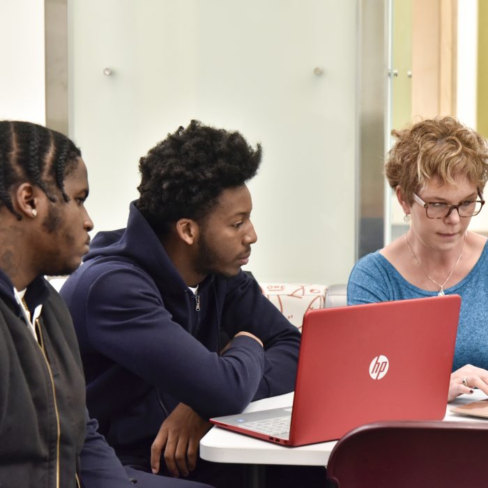 Instructor and two students collaborate around laptops.
