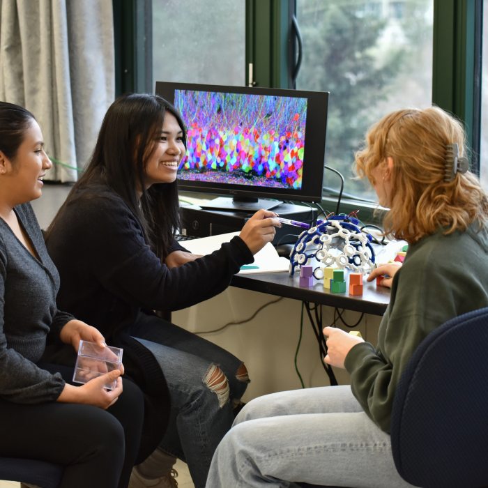 Three psychology students collaborate in a lab or classroom setting.