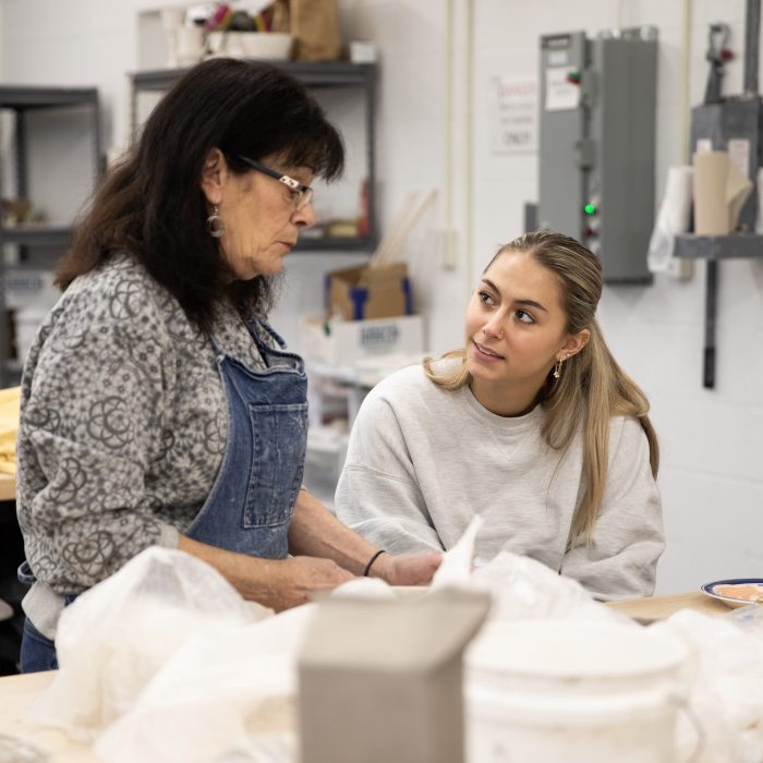 A faculty member guides a ceramics student during a hands-on studio art class.