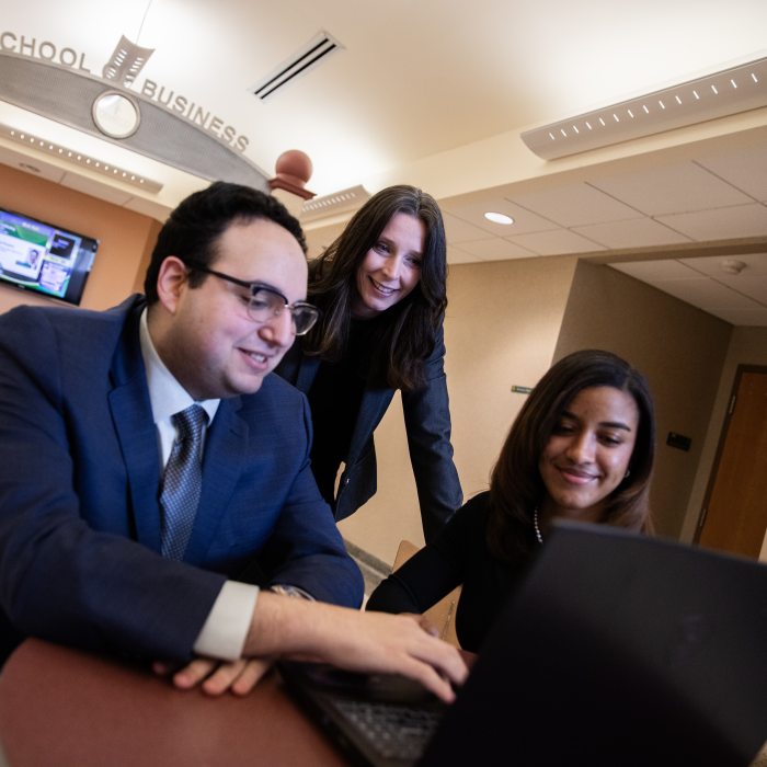 Business students collaborate with a faculty member while reviewing work on a laptop in the School of Business.