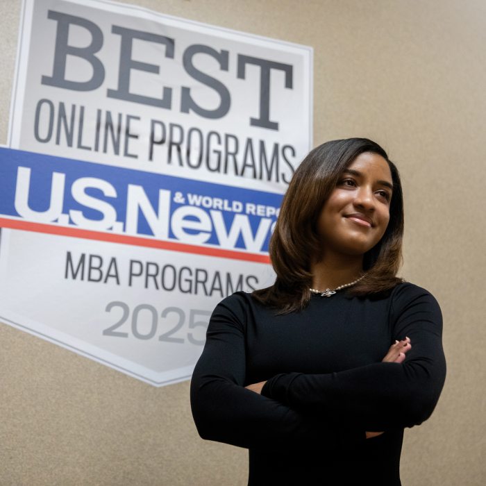 An student stands confidently in front of a U.S. News & World Report Best Online Programs recognition display.