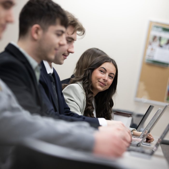 A group of marketing students works on laptops during class, collaborating and engaging in discussion in a professional learning environment.
