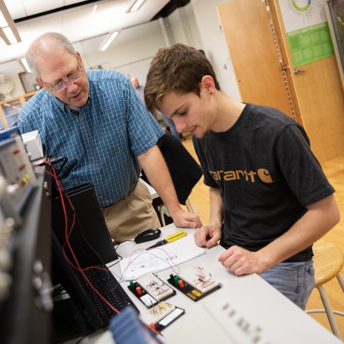 An instructor assists a student working on an electronics circuit project during an electronics technology class.