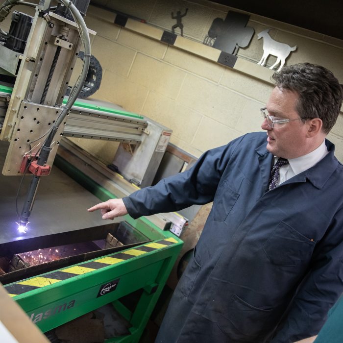 A professor and student working with advanced manufacturing equipment to a student in a technical education lab.