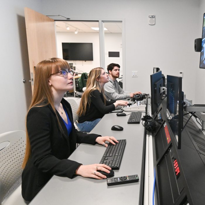Students in a broadcasting studio control room looking at monitors.