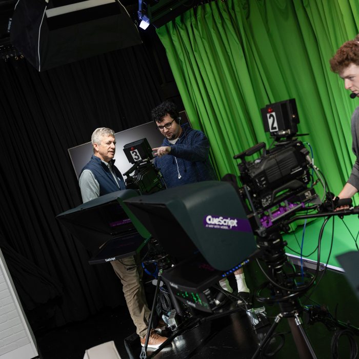 Faculty member with students in broadcasting studio.