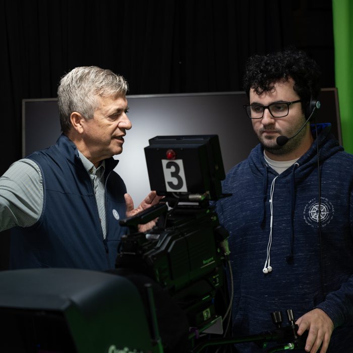 A faculty member instructs a student in a television production studio.