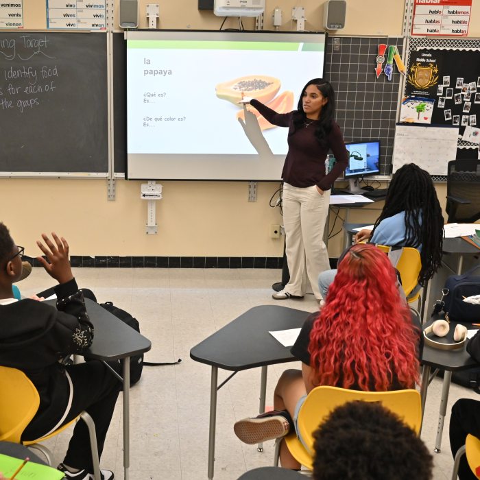 Graduate student teacher at the front of a classroom points to a projected slide