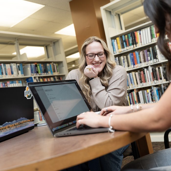 A strategic communication student collaborate on a project in the library.