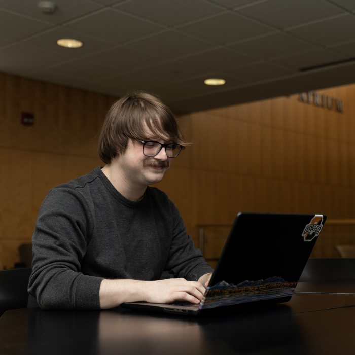 A Higher Education Leadership student works independently on a laptop in a campus learning space.