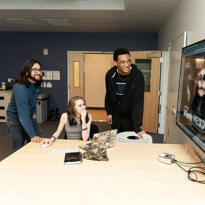 Three students work together on an interaction design project on a large display.