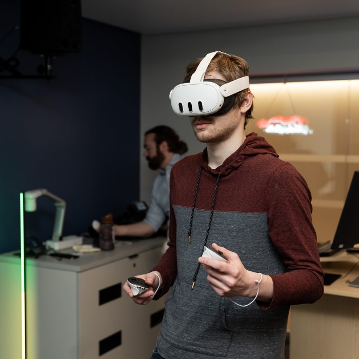 A student uses a virtual reality headset and hand controllers to explore immersive technologies in a human-computer interaction learning environment.