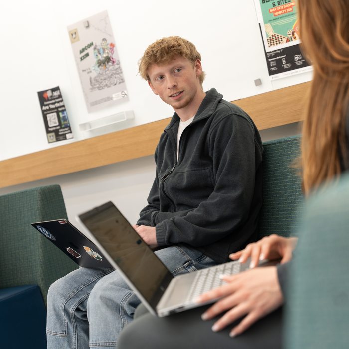 A public relations student collaborates with a classmate while working on laptops.