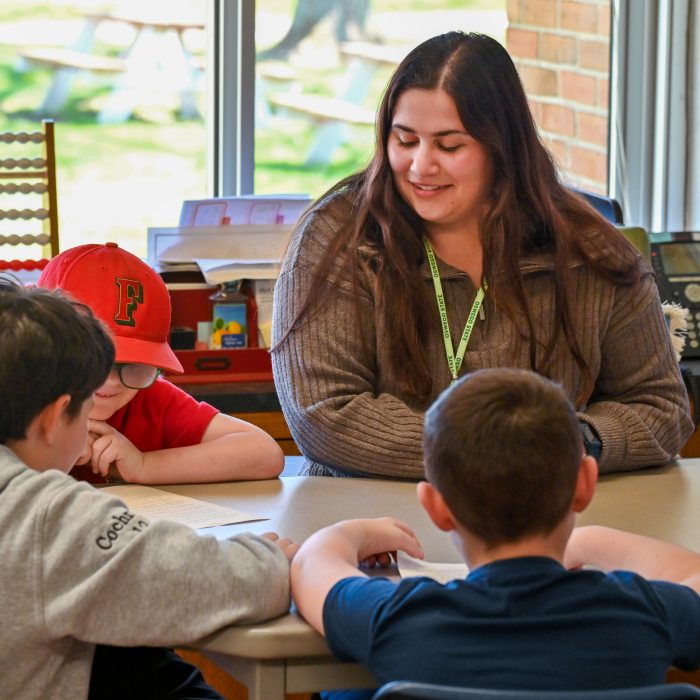 Undergraduate student teacher sitting at a table with three children.