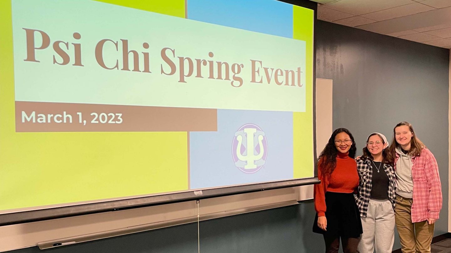 Three students pose in front of Psi Chi Spring event 2023 banner