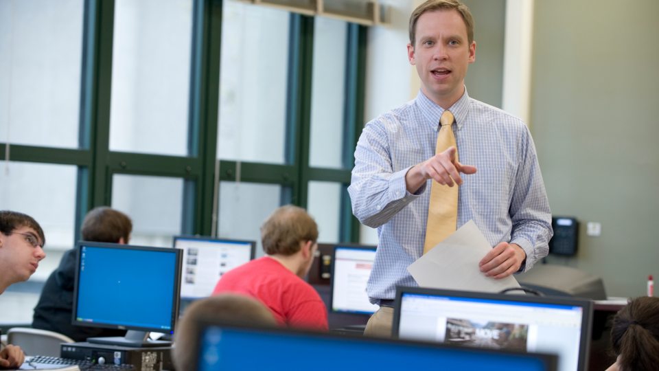A professor standing in the midst of students sitting at desks
