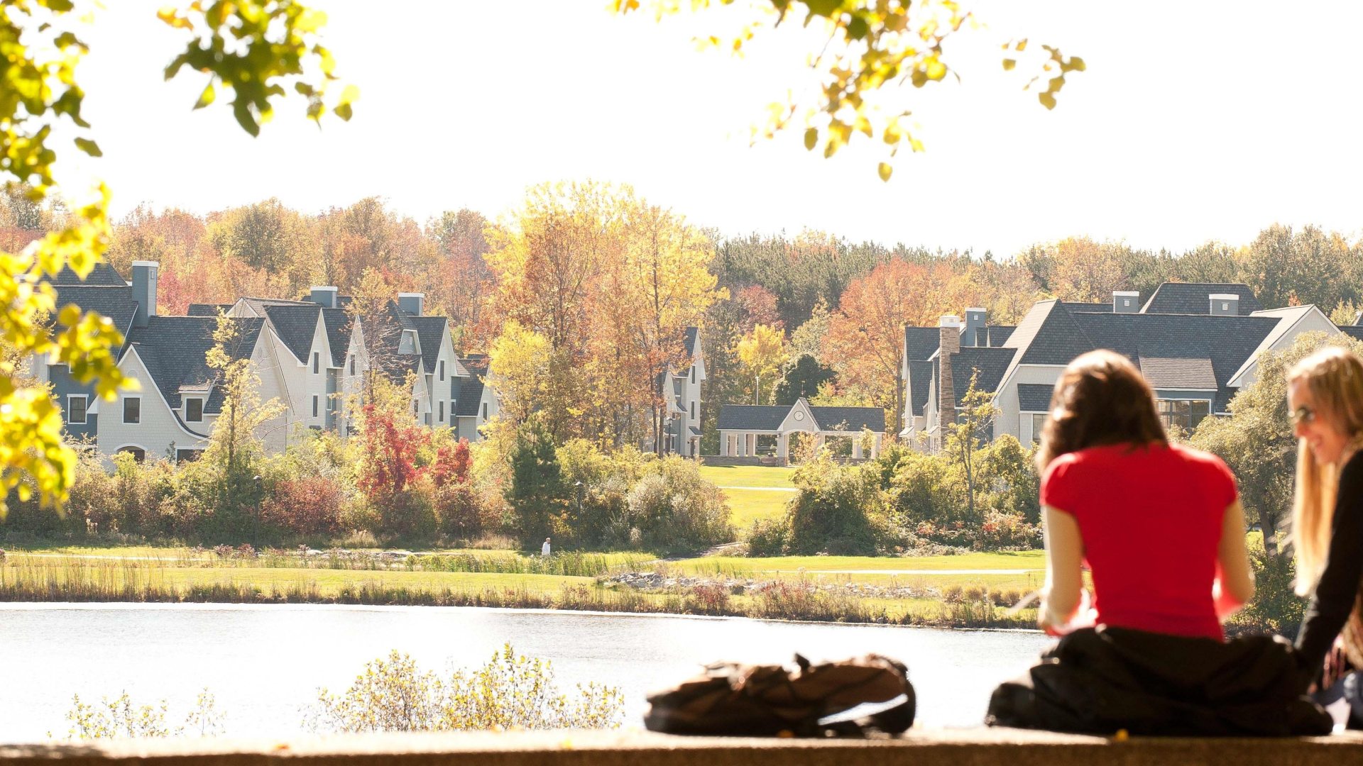 Two students sitting outside by the lagoon, with the Village housing in the distance